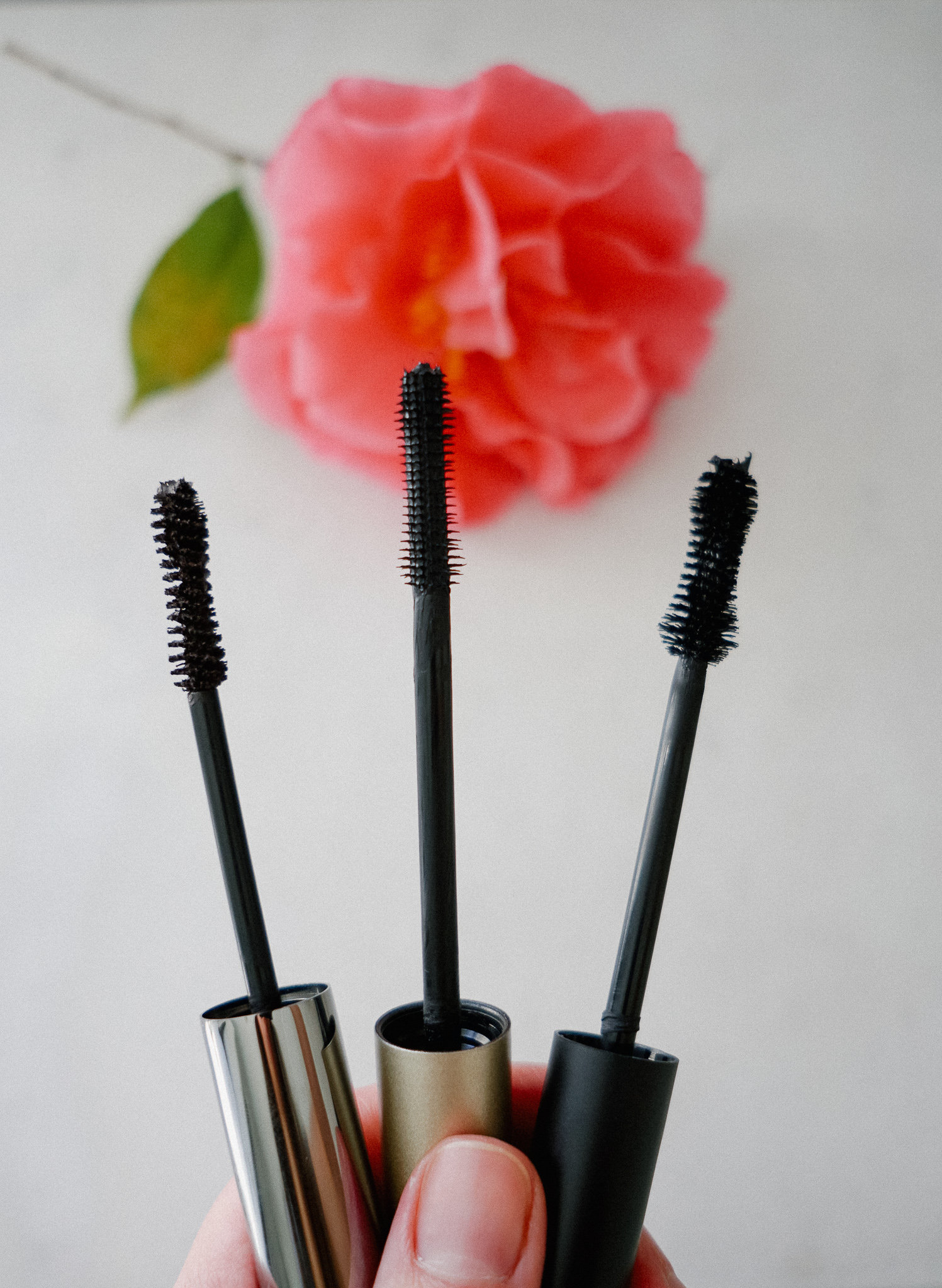 Holding 3 mascara wands out over a flower
