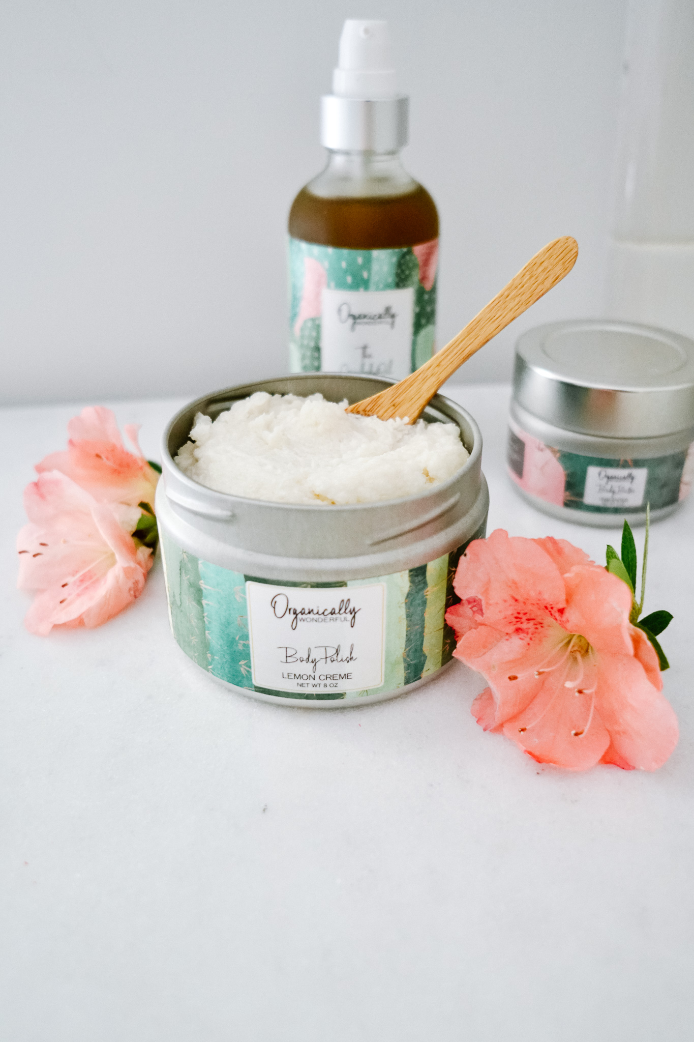 Organically Wonderful Body Scrub open on counter with flowers and other products behind it