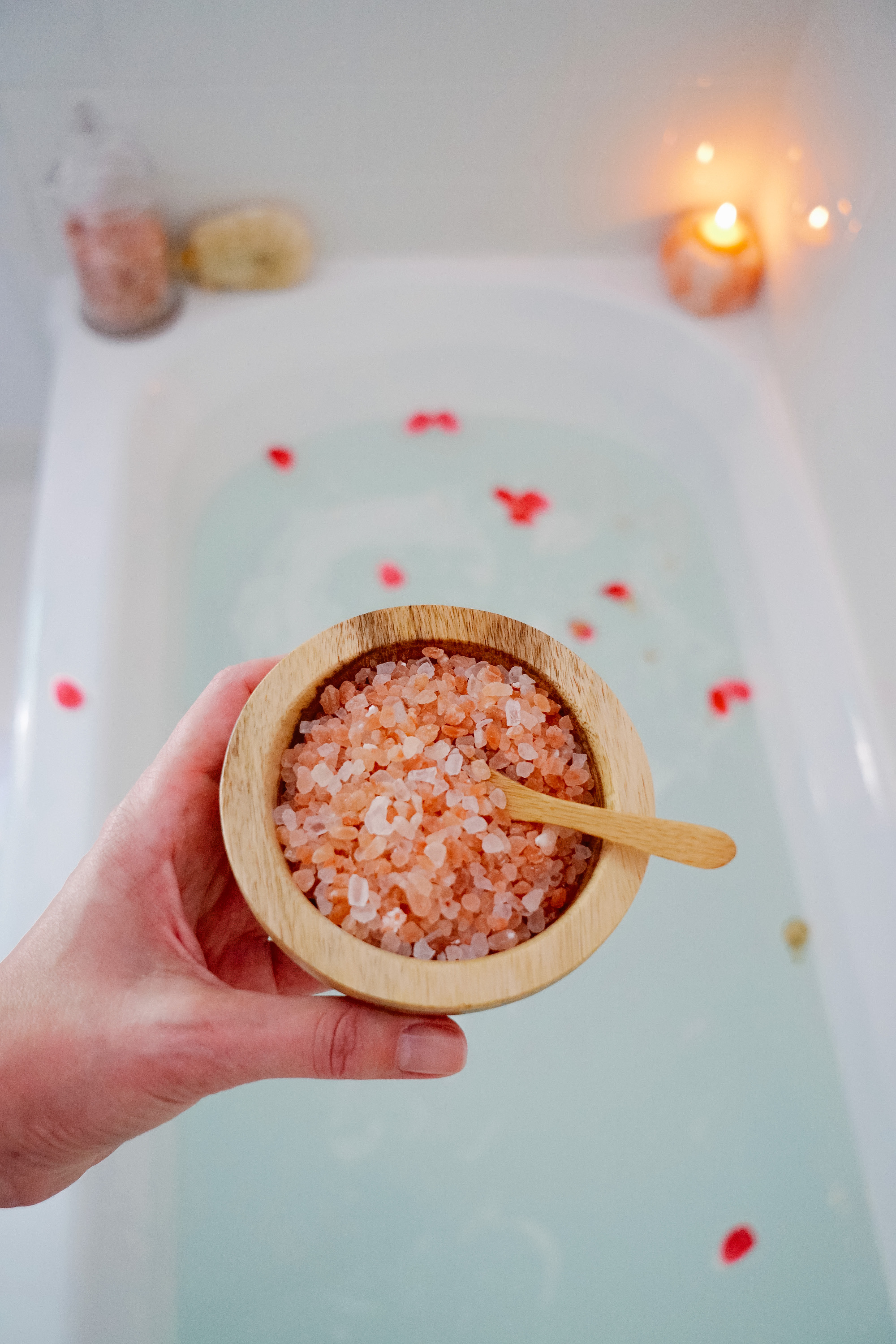 Holding a bowl of pink salt above bath full of water