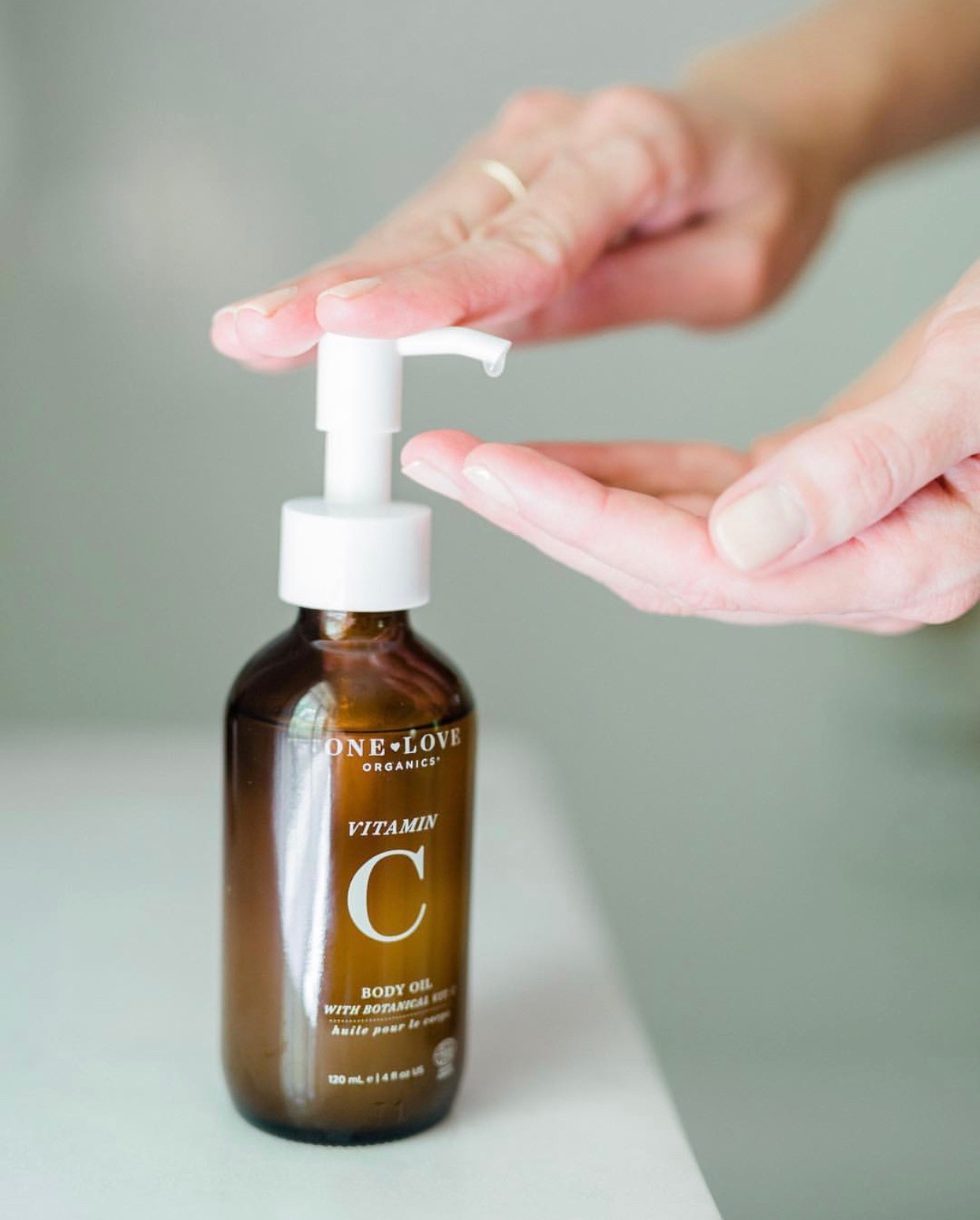 A bottle of body oil on the counter with hands pressing down the pump